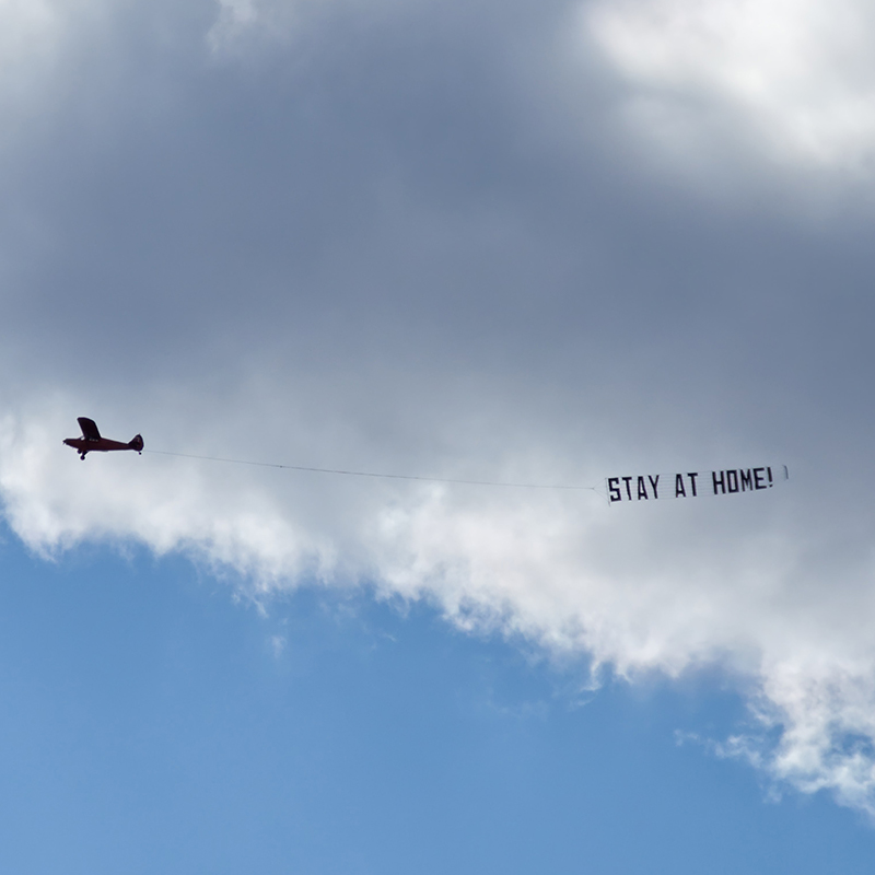 airplane flying and towing a sign behind it that says "stay at home"